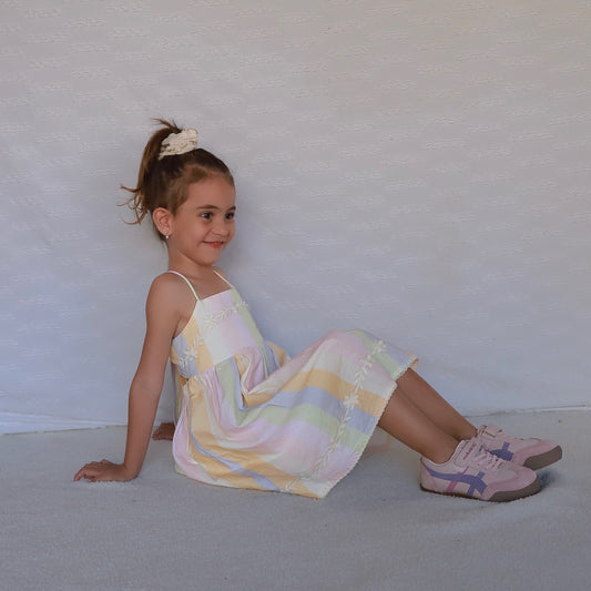 linen and cotton high end design   floor  wearing a pastel striped spaghetti-strap dress and pink sneakers.